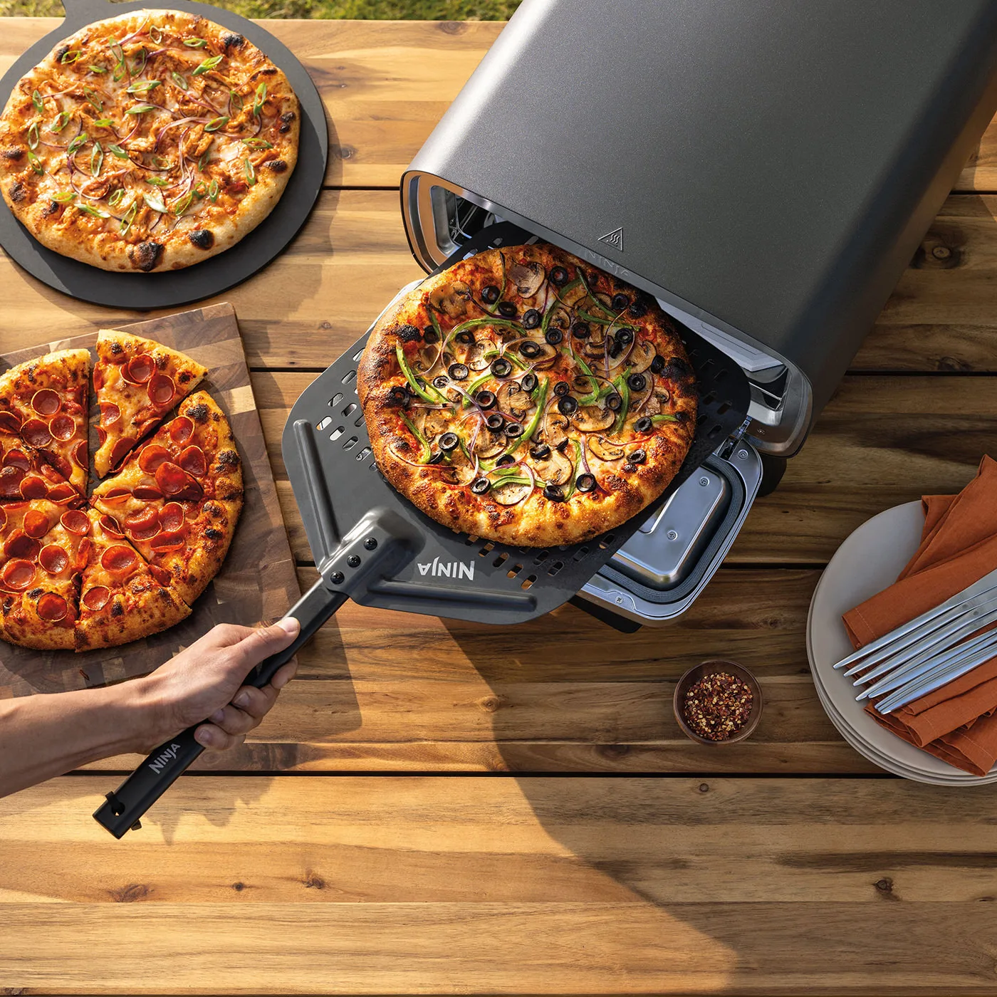 Ninja-MO201UK-InUse-BackYard-OnTable-3-Pizzas-Man